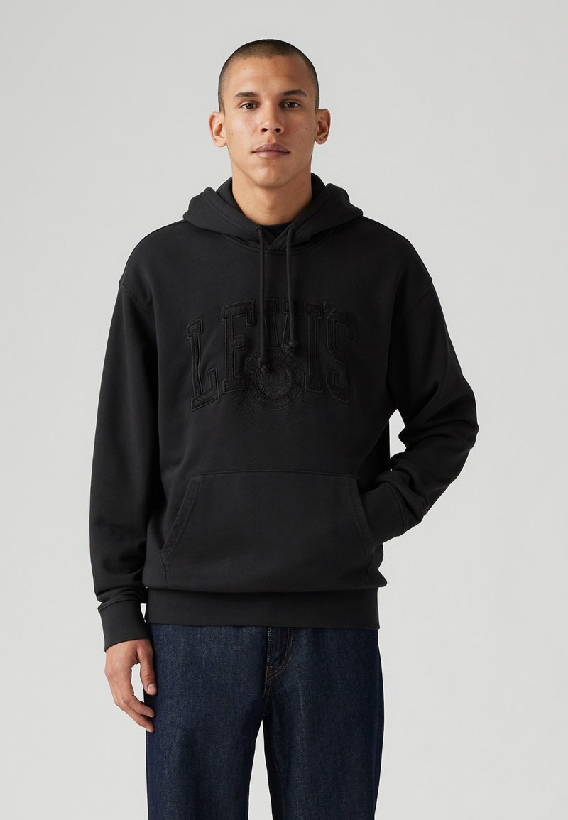 Black hoodie with kangaroo pocket, featuring embossed "LEVI’S" logo on chest, drawstrings on hood, and ribbed cuffs. Paired with dark jeans.