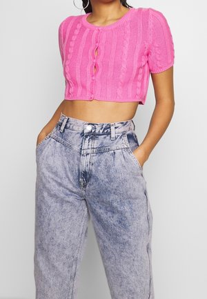 Vaaleanpunainen lyhyt neulejakku, jossa on palmikkoneulekuvio, lyhyet hihat ja edessä nappikiinnitys. Yhdistetty korkeavyötäröisiin vaaleansinisiin farkkuihin.