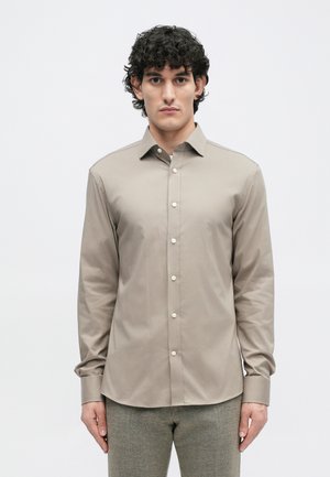 Camisa de manga larga beige con cuello abotonado y botones en la parte delantera, fabricada en una tela suave. Presenta un corte entallado y un ligero brillo.