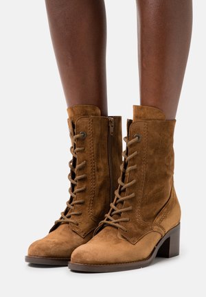 Ruske nubuk ankle boots z okroglo konico, zavezovanjem spredaj in stranskim zadrgo, ki imajo zložen peto in kontrastne šive.