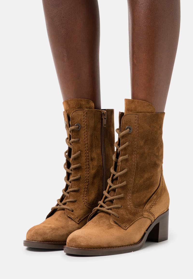 Hnědé semišové kotníkové boty s kulatou špičkou, šněrováním vpředu a postranním zipem, s vrstvovou podrážkou a kontrastními švy.