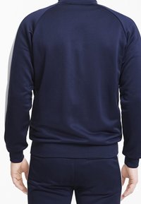 Námořnická modrá mikina s vysokým límcem, žebrovanými manžetami a lemem. Tkanina má hladkou texturu a jednoduchý, zakřivený design.