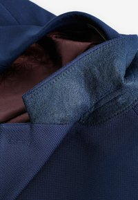 Marinefarbener Stoffjacke mit strukturierter Außenschicht und glatter Innenauskleidung in einem kastanienroten Farbton. Auffälliger Filzkragen und sorgfältige Nahtdetails.