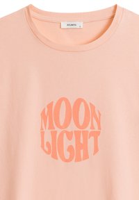 Brzoskwiniowa bawełniana koszulka z okrągłą grafiką "MOON LIGHT" w kontrastującym koralowym kolorze, o miękkiej fakturze i okrągłym dekolcie.