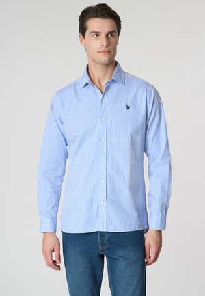Camicia button-up a quadri blu chiaro con maniche lunghe, bottoni bianchi e un piccolo logo ricamato sul petto. Indossata con jeans blu.