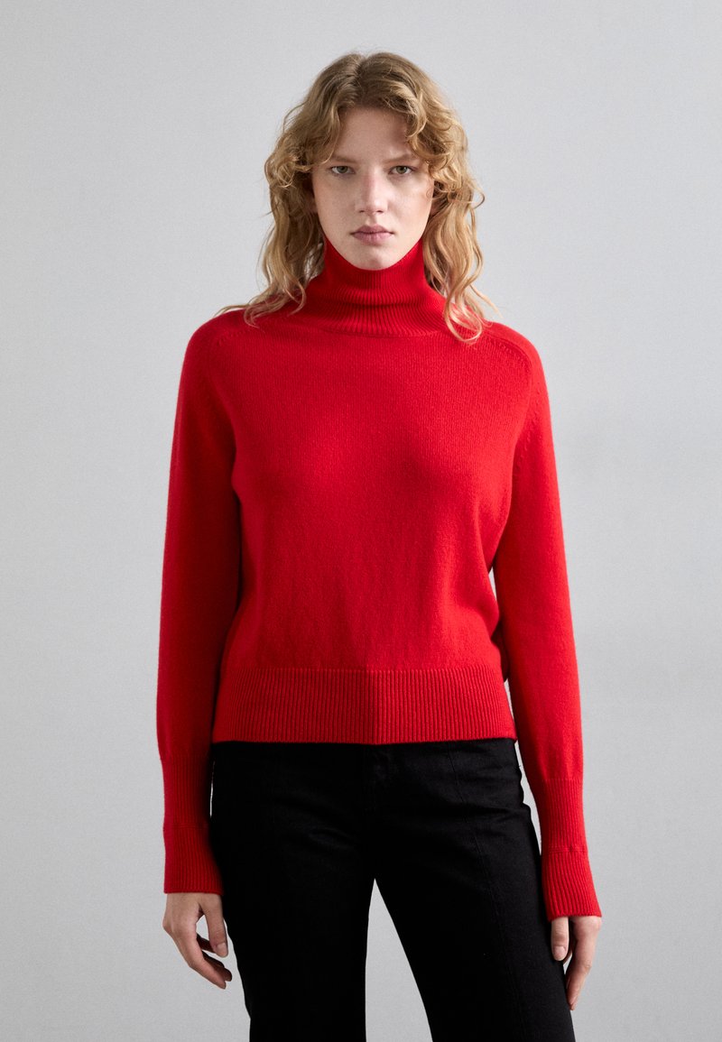 Punainen poolopaita pehmeästä kankaasta, jossa on ribbireunat hihoissa ja helmassa, slim fit -malli ja pitkät hihat.
