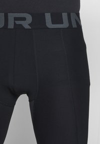 Sorte atletiske leggings med en tætsiddende design, der har en grå elastisk talje med skrift og en glat, struktureret stof.