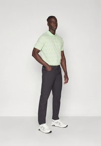 Polo vert clair à motif, pantalon noir et baskets blanches. Le polo présente un dessin géométrique subtil et un col classique.