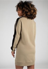 Vestido de sudadera beige con franjas laterales negras, de mangas largas y corte relajado. Textura suave y detalles en los puños acanalados.