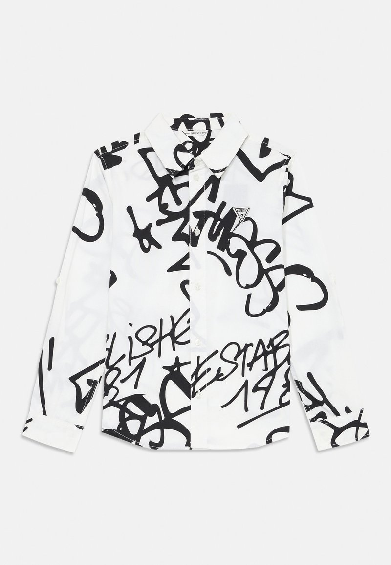 Chemise blanche à manches longues avec boutons, ornée de textes et de dessins abstraits en style graffiti noir, avec un petit logo triangulaire Guess sur la poitrine.