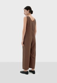Bruine gestreepte jumpsuit met brede pijpen, mouwloos ontwerp, ronde rug en subtiele textuur. Styled met zwarte platte schoenen en zilveren oorbellen.