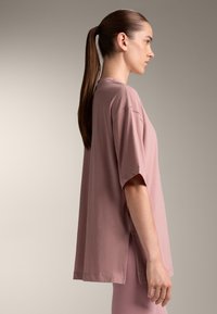 Oversized short-sleeve t-shirt in soft pink cotton, featuring side slits and a relaxed fit. Smooth texture, minimal stitching detail.