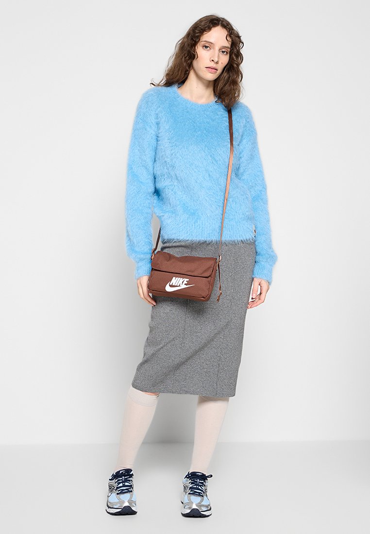 Suéter azul claro y peludo, falda midi gris, bolso cruzado marrón con logo blanco de Nike, calcetas blancas hasta la rodilla y zapatillas azules.