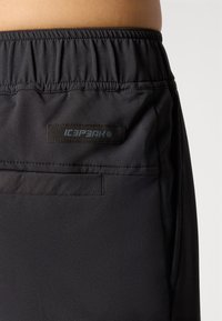 Zwarte shorts met elastische tailleband, voorzien van een zijzak en een zwart logo label. Het materiaal lijkt glad met een subtiele textuur.