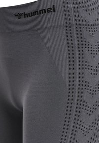 Szare legginsy sportowe z prążkowanym paskiem w talii i teksturowanym wzorem po bokach, z perforowanymi akcentami dla lepszej oddychalności.
