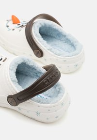 Zoccoli bianchi con una morbida fodera blu, caratterizzati da una banda marrone e un design di Olaf, decorati con motivi di fiocchi di neve azzurri all'esterno.