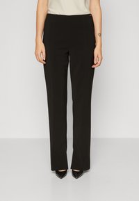 Black tailored trousers featuring a straight leg design, smooth texture, and subtle front seam detailing. Paired with pointed black heels.