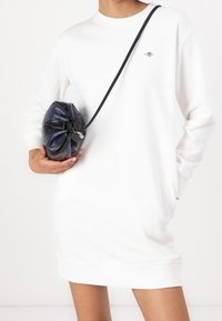 Weißes übergroßes Sweatshirt mit rundem Ausschnitt und gerippten Bündchen, kombiniert mit einer schwarzen und dunkelblauen Kordelzugtasche. Glattes Stoffgefühl.