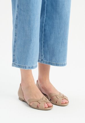 Beige flache Sandalen mit geflochtenem Obermaterial, offenes Zehendesign und niedrigem Absatz, kombiniert mit hellblauen Cropped-Jeans. Glatte Textur und minimale Akzente.