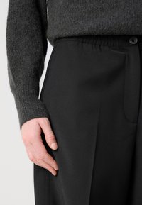 Gray knit sweater with a textured finish, paired with black trousers, featuring a smooth fabric and an elastic waistband with a button detail.