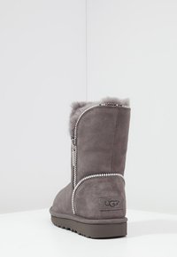 Šedá semišová kotníková bota s kožíškovou podšívkou, bočním zipem a ozdobným lemováním z kamínků podél švu, s texturovanou gumovou podrážkou.