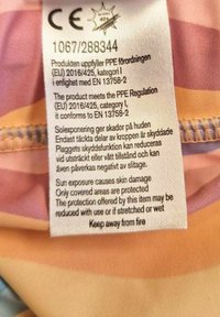 Label featuring care instructions, written in multiple languages. Text is printed on fabric with a colorful, soft background.