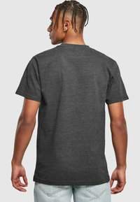 Tumši pelēks kokvilnas t-krekls ar īsām piedurknēm un apaļu kakla izgriezumu, ar gludu tekstūru un brīvu piegriezumu. Nav redzamu dizainu vai grafikas.