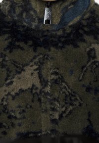 Grün und schwarz gemusterter Fleece mit hohem Kragen, ausgestattet mit einem Reißverschluss und einer plüschigen Textur, der ein Bergmotiv zeigt.