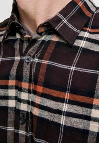 Overhemd van flanel met knopen, voorzien van een geruit patroon in donkerbruin, oranje en crème. Gemaakt van textuurstof met een standaard kraag en knoopsluiting.