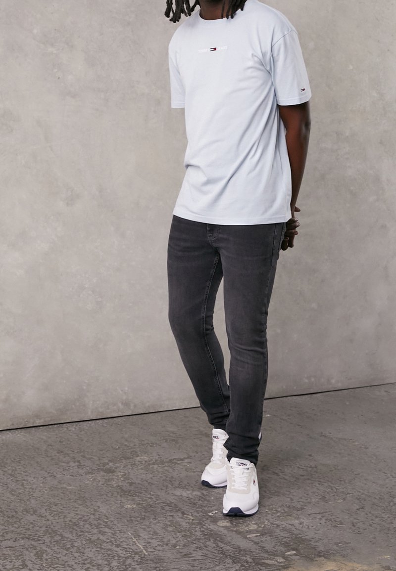 Camiseta de manga corta azul claro con un logo, combinada con jeans oscuros ajustados y zapatillas blancas con detalles en azul marino.