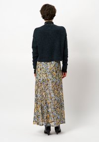 Un pull court sombre en matériau doux associé à une longue robe fluide à fleurs avec un motif coloré dans des tons de bleu et de jaune. Des escarpins noirs.