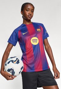 FC Barcelona mez, amely kék és piros csíkokkal, arany kiegészítőkkel, rövid ujjú, valamint a Spotify logóval készült, egy fehér és kék focilabdával párosítva.