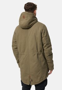 Parka verde oliva con cappuccio, chiusura con bottoni nella parte inferiore e dettaglio logo in pelle sul retro. Presenta un taglio dritto e tessuto testurizzato.