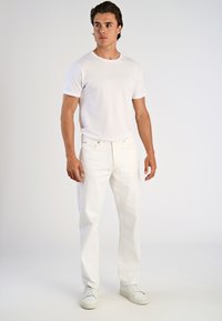 Camiseta blanca de cuello redondo combinada con jeans de mezclilla blancos y zapatillas blancas. El conjunto presenta un diseño simple y limpio, sin patrones.