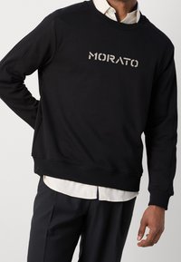 Sweatshirt noir avec poignets et ourlet côtelés, arborant un logo "MORATO" brodé en couleur contrastante. Tissu doux et texturé.