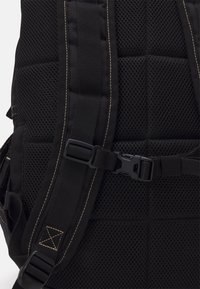 Μαύρος σακίδιο πλάτης με επενδυμένο πλέγμα, ρυθμιζόμενους ιμάντες και πλαστικό κούμπωμα. Οι ραφές προσδίδουν ανθεκτικότητα και δομή.