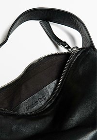 Black leather handbag interior featuring a zip closure, smooth texture, and subtle embossed logo. Strap connected at the top.