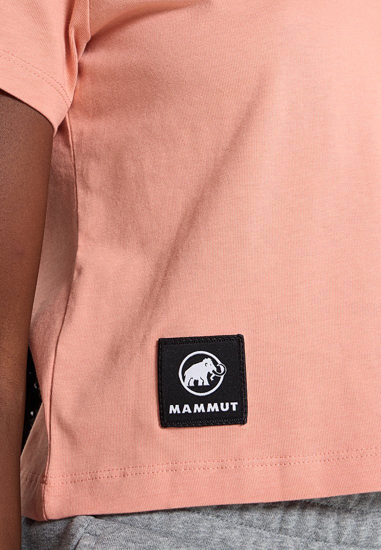 Różowa koszulka z krótkim rękawem wykonana z bawełny, z czarną naszywką w kształcie kwadratu przedstawiającą stylizowanego słonia oraz napisem "MAMMUT".