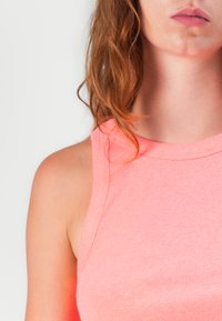 Light pink ribbed sleeveless top with a high neckline, showcasing a smooth texture and fitted design, highlighting shoulder contours.