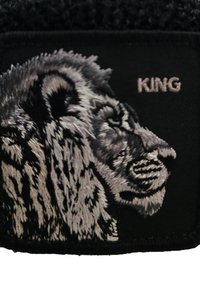 Patch in tessuto nero con una testa di leone ricamata in toni di grigio, accompagnata dalla parola "KING" ricamata in grigio chiaro.