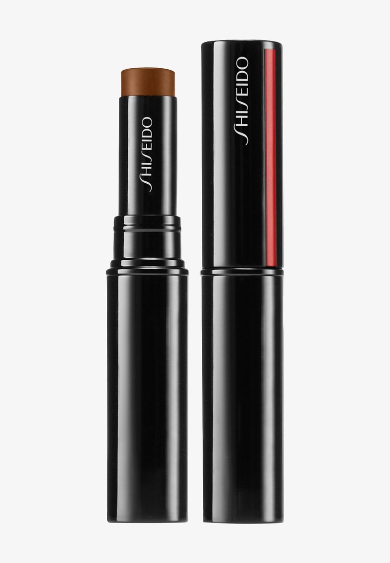Base en barra de Shiseido en un tubo negro retráctil con una punta aplicadora marrón. El tubo presenta un sutil acento rojo y un logo.