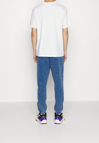 Weißes Baumwoll-T-Shirt kombiniert mit blauen, ausgewaschenen Jogginghosen und bunten Sneakers mit lila, gelben und schwarzen Akzenten.