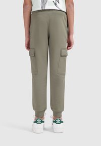Olijfgroene cargobroek met twee zijzakken, elastische boorden en een trekkoord in de taille, gecombineerd met witte sneakers met groene accenten.