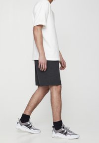 T-shirt en coton blanc, à manches courtes ; short gris foncé avec taille élastique ; chaussures de sport grises et blanches avec accents et lacets noirs.