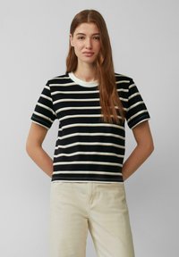 T-shirt à manches courtes noir et blanc rayé avec un col rond et des détails de couture à plat, associé à un pantalon de couleur claire.