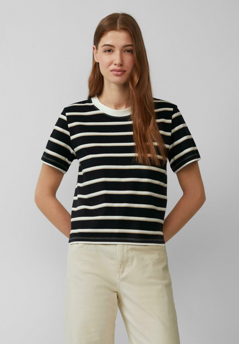 T-shirt à manches courtes noir et blanc rayé avec un col rond et des détails de couture à plat, associé à un pantalon de couleur claire.