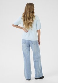 Hellblau strukturiertes Kurzarmoberteil kombiniert mit weit geschnittenen, hellen Jeans. Das Outfit zeichnet sich durch eine lockere Passform und schlichte Designdetails aus.