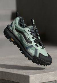 Jasnozielony i czarny but trekkingowy z teksturowaną cholewką, marką Gore-Tex oraz wytrzymałą, wielokierunkową podeszwą gumową.