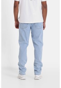 Vaqueros de mezclilla de color azul claro con un corte relajado, diseño de cinco bolsillos y detalles de costura discretos. Llevados con una camiseta blanca de manga corta.