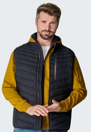 Schwarze, gesteppten Pufferweste mit Reißverschluss-Taschen, über einem senfgelben Hoodie getragen. Verfügt über einen hohen Kragen und eine glatte Stoffbeschaffenheit.